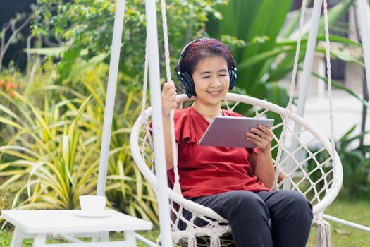 Middle aged woman relaxing on swing listen music on the tablet computer in backyard..