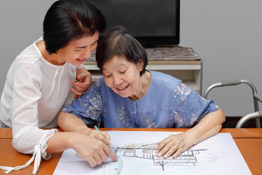 Elderly woman painting color on her drawing with daughter , hobby at home