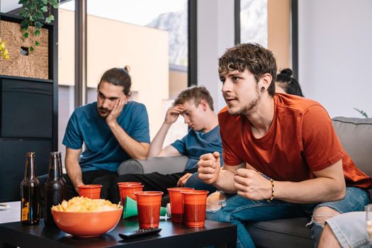 friends jumping for joy after their team's victory, watching football match on TV. opposing team sad after defeat leisure concept, three young adults in blue t-shirts. happy and cheerful. natural light in the living room at home.