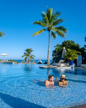Beautiful tropical beachfront hotel resort with a swimming pool, sun-loungers, and palm trees , a paradise destination for vacations. couple men and woman mid age on a luxury vacation