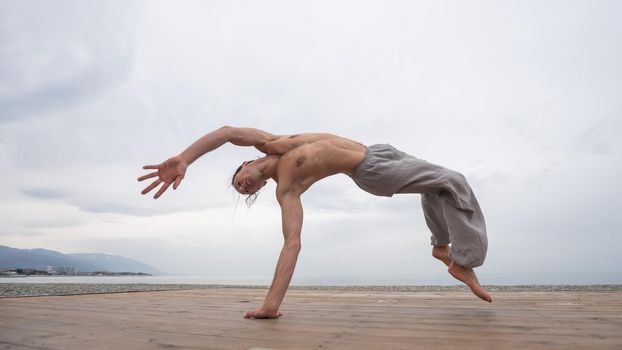 Shirtless caucasian man doing backflip on pebble beach