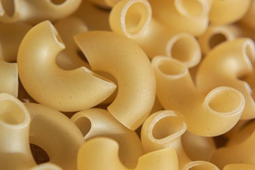 Macaroni raw background. Curved hollow horns for making macaroni cheese. Backdrop for a culinary theme. Selective focus.