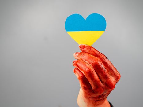 Woman with hands covered in blood holding a heart with the flag of ukraine on a white background