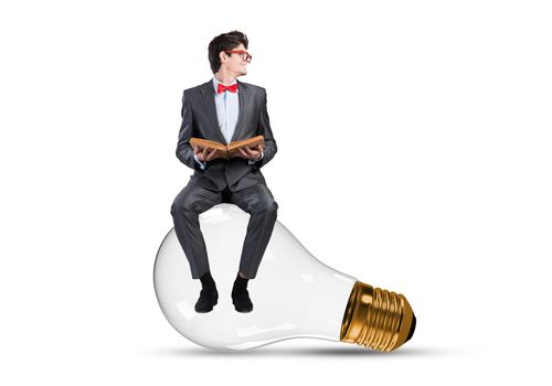 Young businessman sits on an electric light bulb. holds a book in his hands