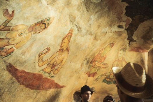 Group of tourists admire the wall painting (frescoes) in Sigiriya an ancient rock fortress , Apsara celestial nymphs - ancient painting on the walls in the Lion Rock cave, Sigiriya, Sri Lanka