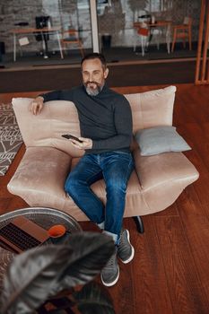 Happy man sitting in comfortable armchair while using smartphone