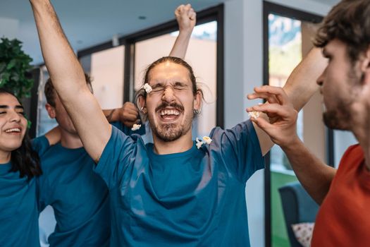 group of friends jumping for joy after the victory of their soccer team. losing team throws popcorn at the winning team. leisure concept. happy and cheerful. natural light in the living room at home. trumpet