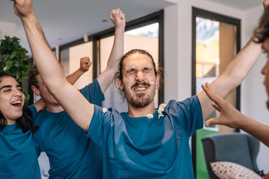 friends jumping for joy after the victory of their e-sports team. losing team throws popcorn at the winning team. leisure concept. happy and cheerful. natural light in the living room at home. trumpet