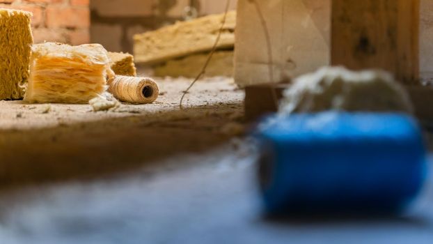 A skein of jute thread licks on the floor near glass wool.Comparison of jute natural eco-friendly thread and blue propylene thread for hemming insulation