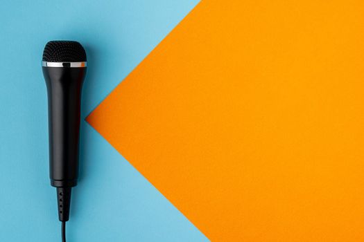 Cable black microphone on colorful blue and orange background, directly above, copy space. Musical professional studio equipment. Modern broadcasting concept. Karaoke entertainment mockup