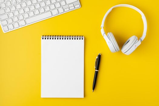 Blank notepad with fountain pen, portable keyboard and headphones on bright yellow background. Workspace office surface. Wireless technology concept, copy space, horizontal, overhead