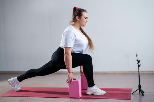 Young Plus Size Woman Stretching At Home Online. Flexible girl practices yoga and watches an online course on a laptop.