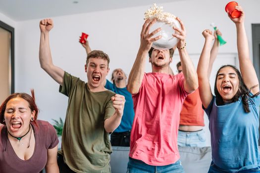 friends jumping for joy, throwing popcorn in the air after their team's victory. group of young people watching football at home. leisure concept. happy and cheerful. natural light in the living room at home. trumpet