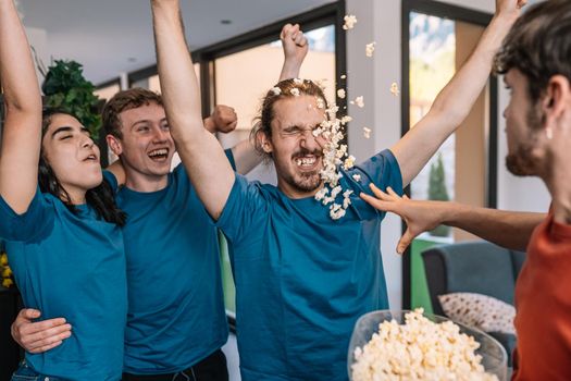 group of friends jumping for joy after the victory of their sports team. losing team throws popcorn at the winning team. leisure concept. happy and cheerful. natural light in the living room at home. trumpet