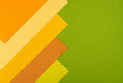 Horizontal of colorful geometric shaped overlapped orange and yellow cardboard layers of paper on green background, copy space, top view. Rectangular design concept