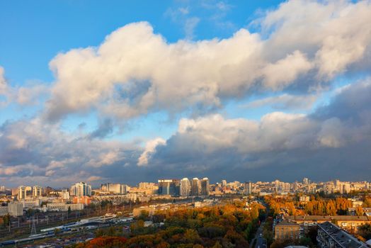 The sun's rays break through gray clouds, exposing the blue of the sky and brightly illuminating the autumn cityscape of Kyiv. Bird's-eye view.