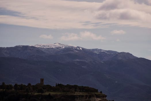 Landscape showing Tona Castle under snowy mountains and cloudy sky in Tona town in Catalonia