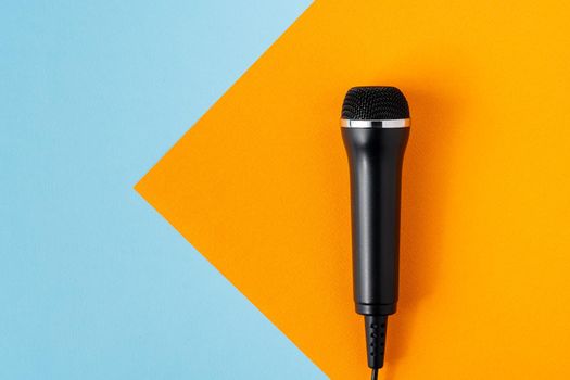 Cable black microphone on colorful blue and orange backdrop, high view angle, copy space. Musical professional studio equipment. Modern broadcasting concept. Karaoke entertainment mockup