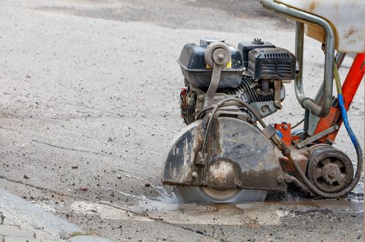 A mobile petrol cutter in the process of work and precisely cuts the asphalt with a diamond cutting disc along the marked line, close-up, copy space.