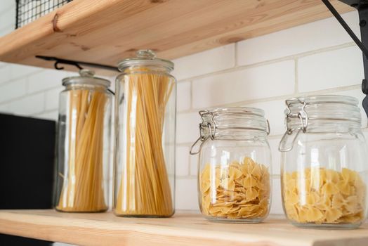 Wheat Italian pasta in glass jar on a wooden shelf in the kitchen