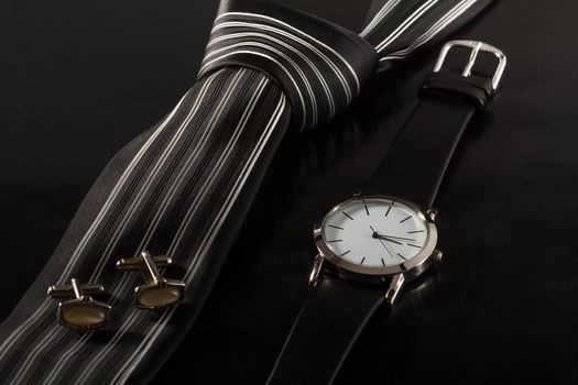 Silk tie, cufflinks, watch with a leather strap on a black background