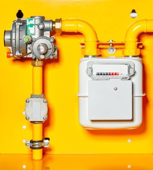 Gas meter, reducer and pipes mounted on a yellow background wall, copy space.