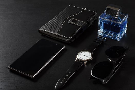 Watch with a leather strap, notebook in leather cover, sell phone, man perfume, sunglasses on a black background