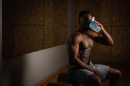 Shirtless african american man drinking from a shaker in the gym