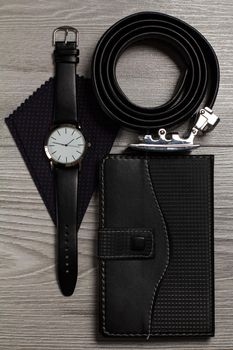 Leather belt with metal buckle, watch with a leather strap, silk handkerchief, notebook in leather cover on a gray wooden background