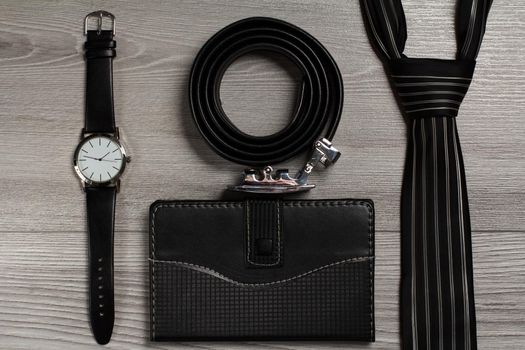 Leather belt with metal buckle, watch with a leather strap, silk tie, notebook in leather cover on a gray wooden background