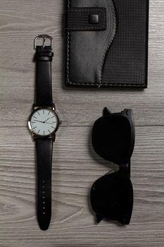 Watch with a leather strap, notebook in leather cover, black sunglasses on a gray wooden background