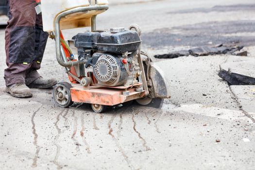 The petrol cutter smoothly cuts the asphalt with a diamond cut-off wheel along the marked line. Close-up, copy space.