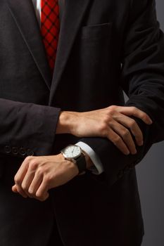 Young man in a suit and red necktie is standing and looking at his watch