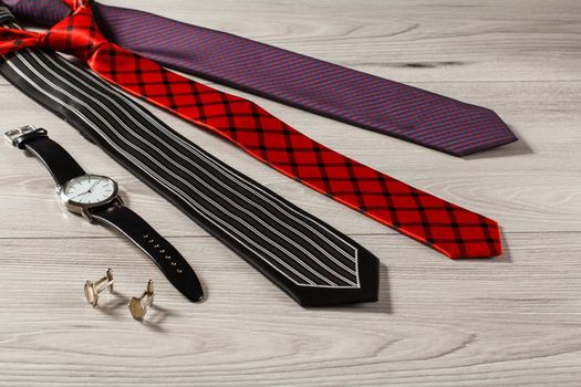 Black, red and violet silk neckties, watch with a leather strap, cufflinks on a gray wooden background