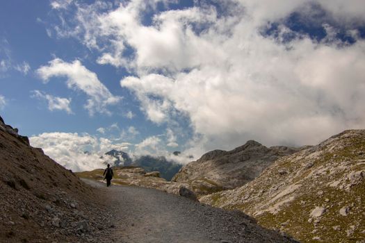 A girl walking on a path surrounded by some mountains under some clouds in a beautiful landscape in Fuente De in Spain