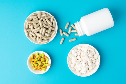 Horizontal of large group of assorted colorful capsules, pulls, tablets in bowl and bottle on blue background. Concept of pharmaceutical treatment. Healthcare remedy supplements