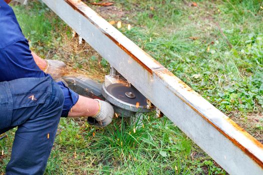 The worker cuts the metal channel with a disc angle grinder with an abrasive reinforced disc, creating a bright plume of many hot sparks.