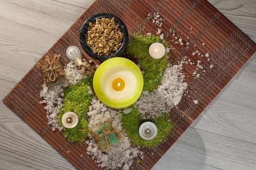 Spa accessories with soap, bowl with dried chamomile flowers, bottles with aromatic oil, sea salt, candles on bamboo napkin