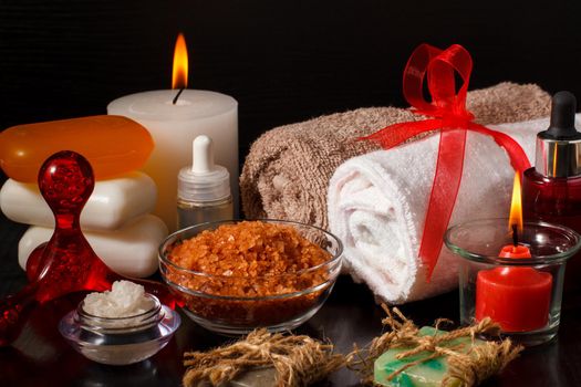 Spa products with soap, bowls with sea salt, bottles with aromatic oil, candles and towels on black background