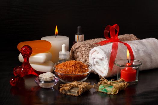 Spa products with soap, bowls with sea salt, bottles with aromatic oil, candles and towels on black background