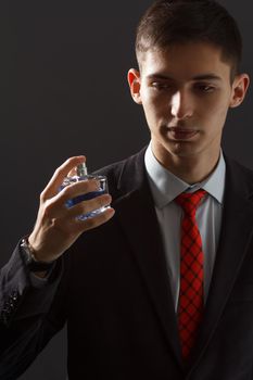 Young man in black suit and red necktie holding man perfume in his hand