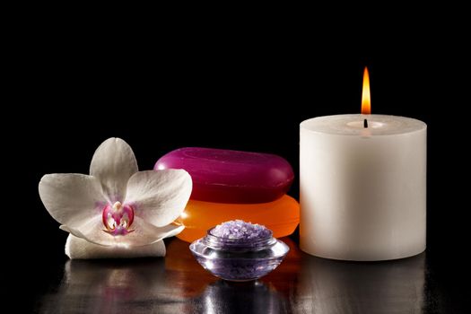 White orchid flower, soap, bowl with sea salt for spa, candle on black background