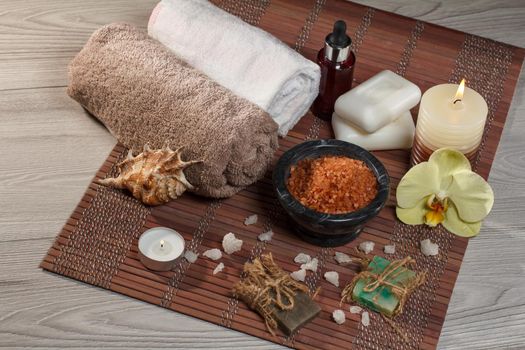 Spa setting with orchid flower, bowl with sea salt, seashell, bottle with aromatic oil, soap, candles and towels on bamboo napkin
