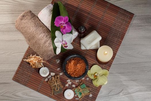 Spa and wellness setting with orchid flowers, bowl with sea salt, seashell, bottle with aromatic oil, soap, candles and towels on bamboo napkin