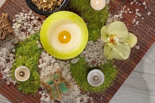Spa accessories with soap, yellow orchid flower, bowl with dried chamomile flowers, bottles with aromatic oil, sea salt, candles on bamboo napkin