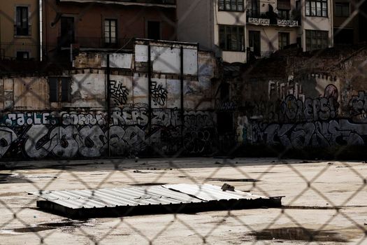 Street walls plenty of graffiti viewed through a fence in Barcelona