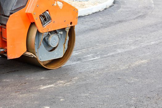 The metal cylinder of a large vibratory roller powerfully compacts the fresh asphalt of the road surface. Close-up, copy space.