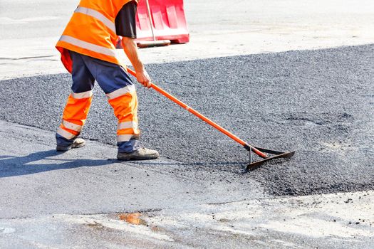 While repairing the road, the road builder levels the fresh asphalt with a metal level against the background of smooth fresh asphalt. Copy space, selective focus.