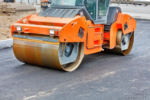 The metal cylinders of the large vibratory roller roll over the new road surface for powerful compaction of the fresh asphalt.