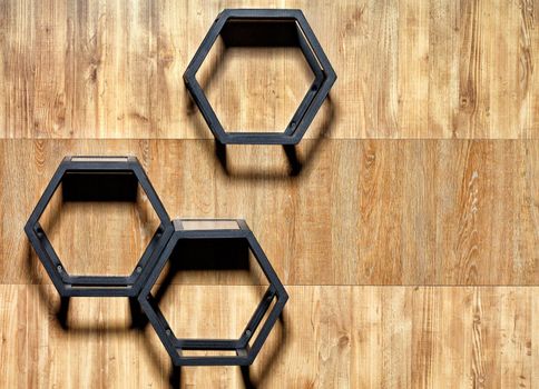 Metal black cubic stylish shelves with hex cutouts on a wooden wall background, copy space.